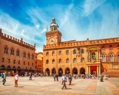 Italy Piazza Maggiore in Bologna old town tower of town hall with big clock and blue sky on background, antique buildings terracotta galleries