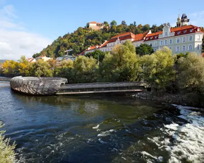 River Mur with the artificial floating platform Mur island (Murinsel) in the middle and old buildings on the river bank. Graz, Austria.