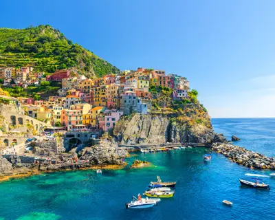 Manarola traditional typical Italian village in National park Cinque Terre, colorful multicolored buildings houses on rock cliff, fishing boats on water, blue sky background, La Spezia, Liguria, Italy