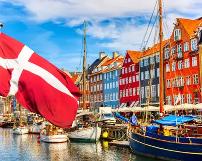 Copenhagen iconic view. Famous old Nyhavn port in the center of Copenhagen, Denmark during summer sunny day with Denmark flag on the foreground