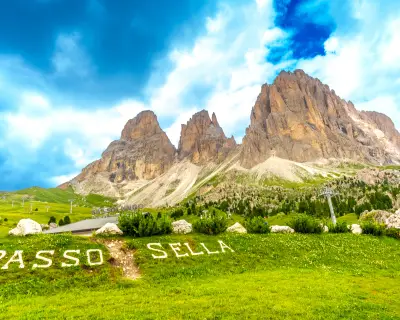Green meadow with passo sella sign and the sassolungo group in the background, dolomites, italy